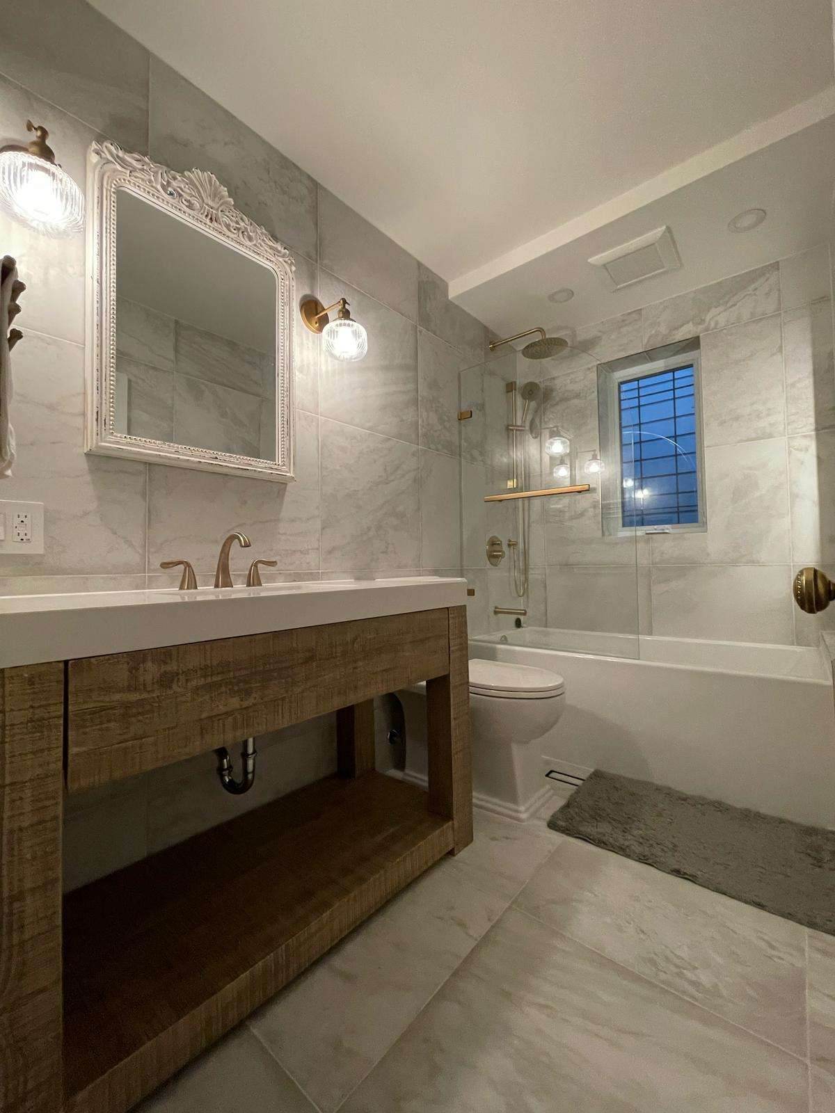 Finished basement bathroom with marble tile, wood vanity and brass fixtures