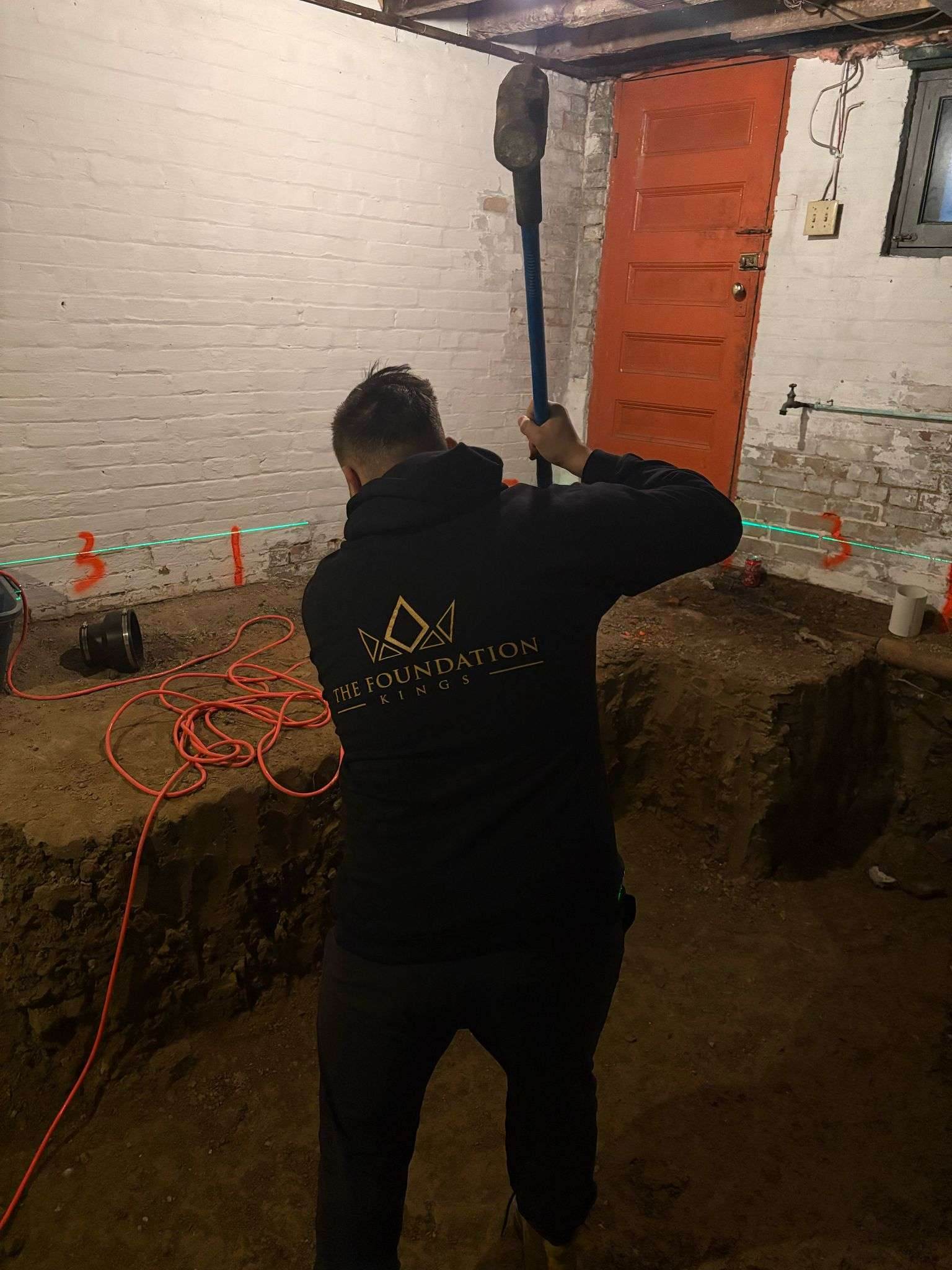 Foundation Kings worker in a branded sweater excavating a Toronto basement floor