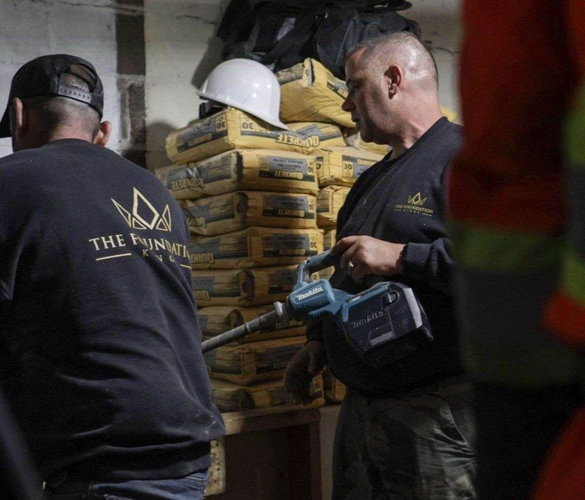 Foundation Kings foreman in a branded sweater preparing materials for basement underpinning