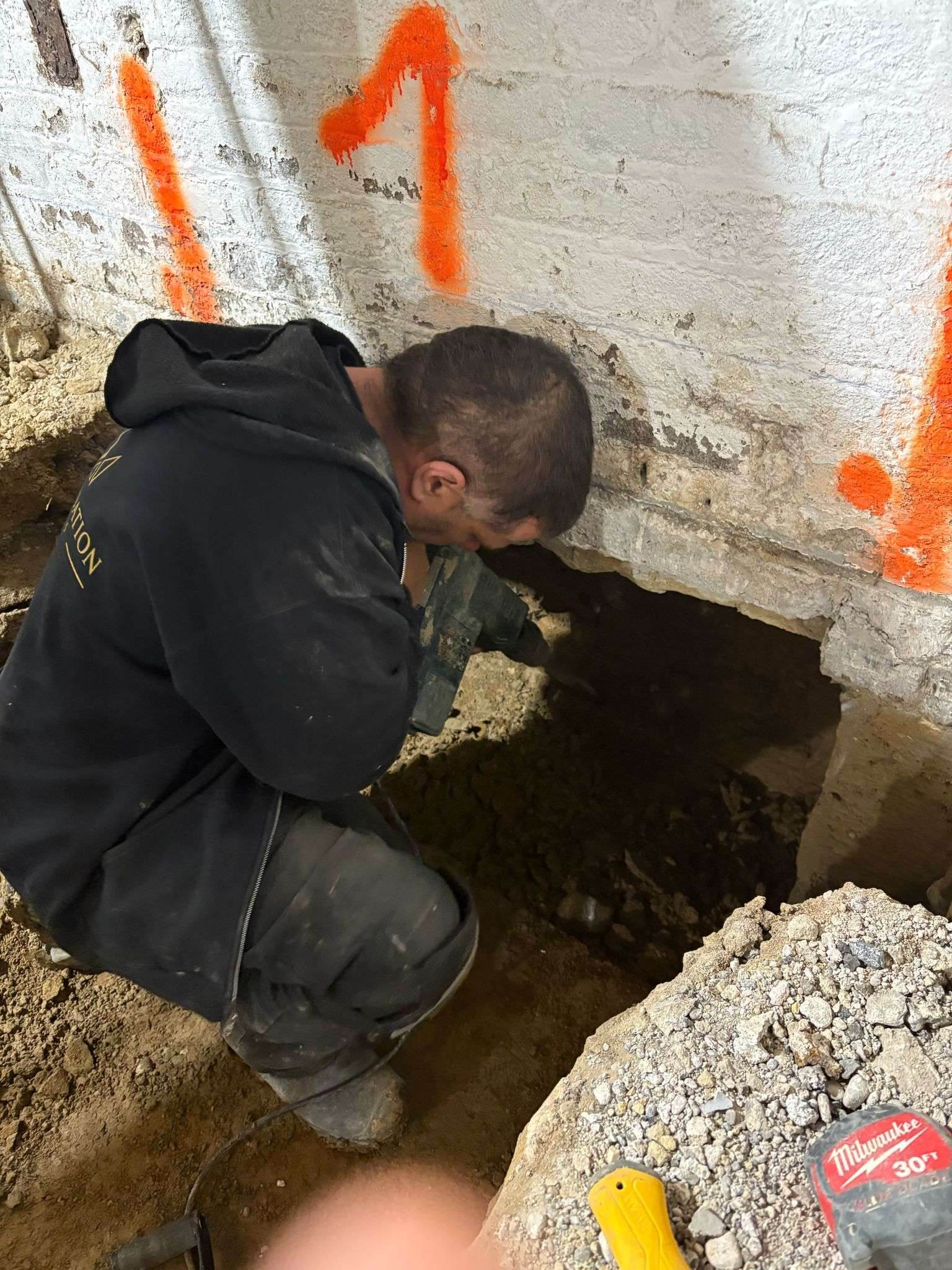 Foundation Kings worker hand-digging an underpinning pin under a numbered foundation wall