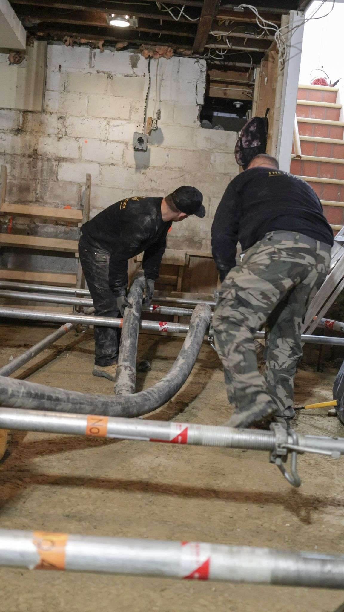 Crew pumping concrete into underpinning pins beneath a Toronto house