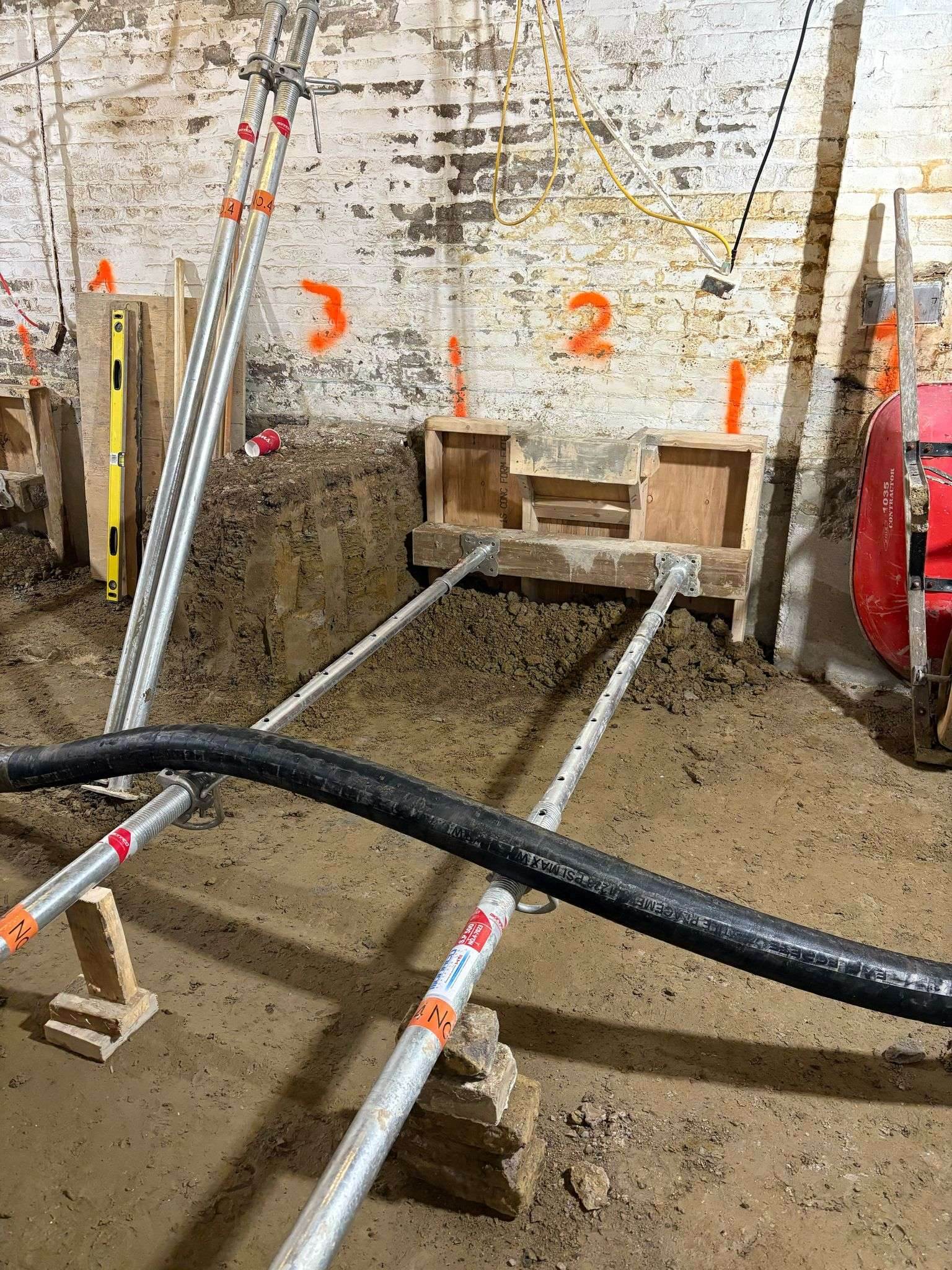 Underpinning pins with shoring posts and a concrete hose in a Toronto basement